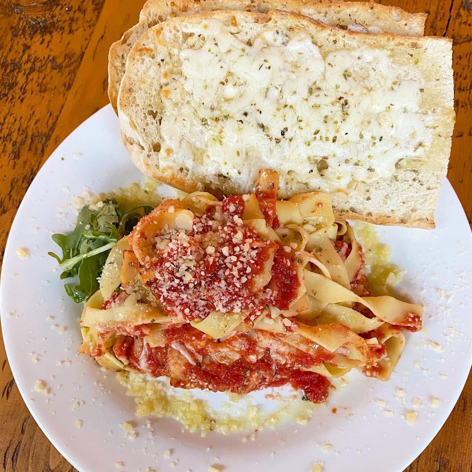 Plate of ribbon pasta with tomato sauce, grated cheese, and cheesy herb bread on a wooden table.